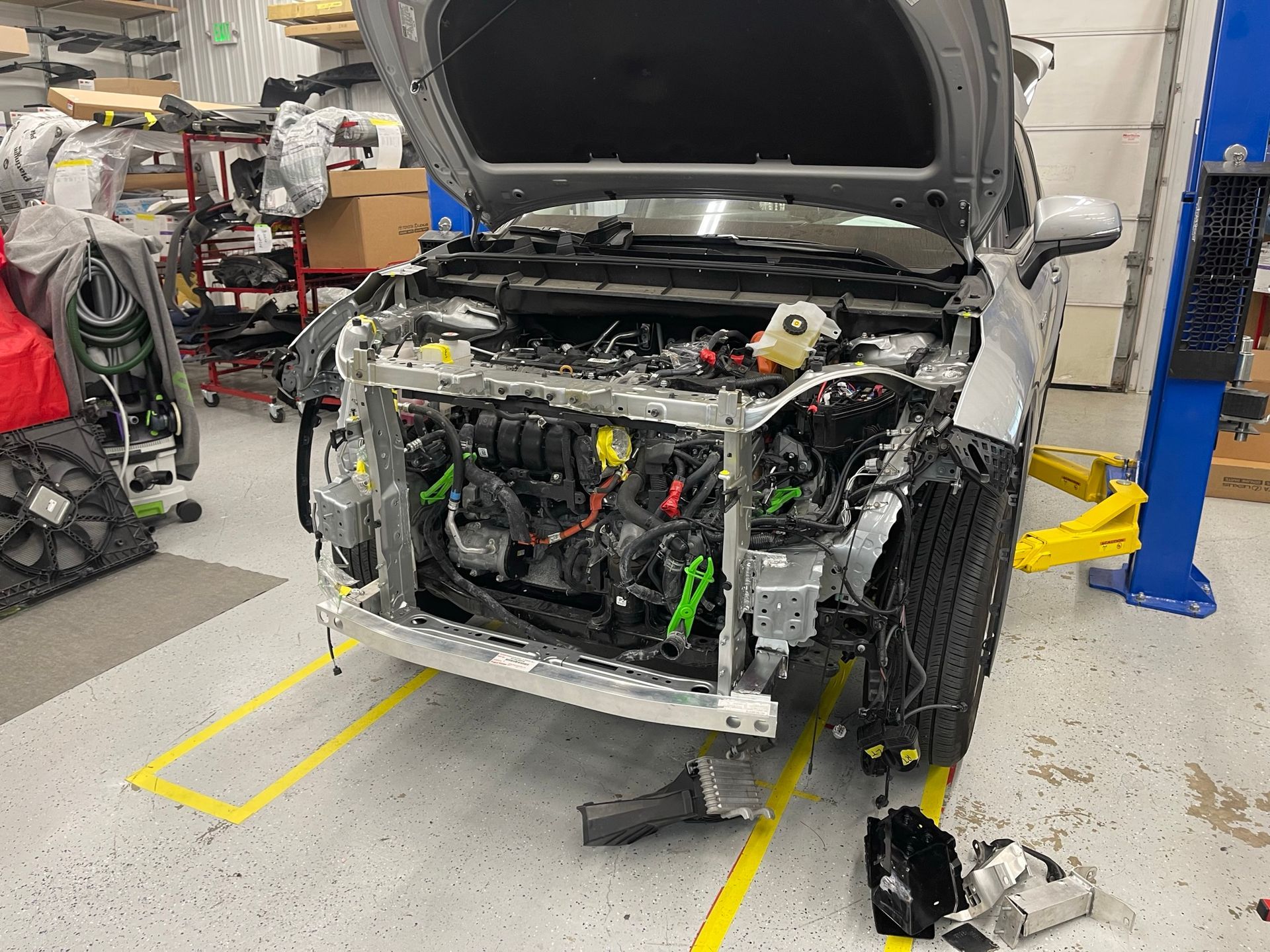 A car is being repaired in a garage with the hood up.