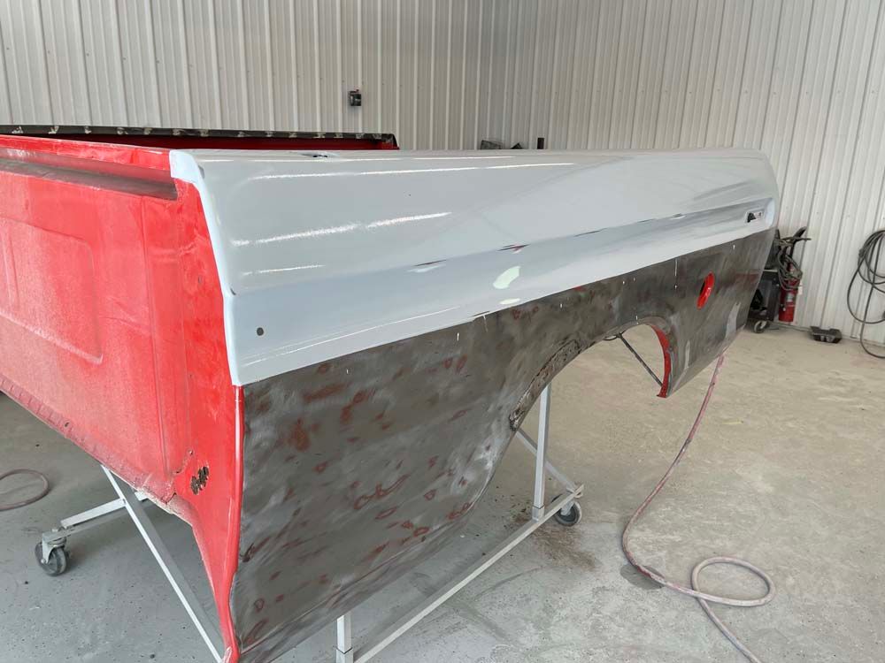 A red and white truck bed is being painted in a garage.
