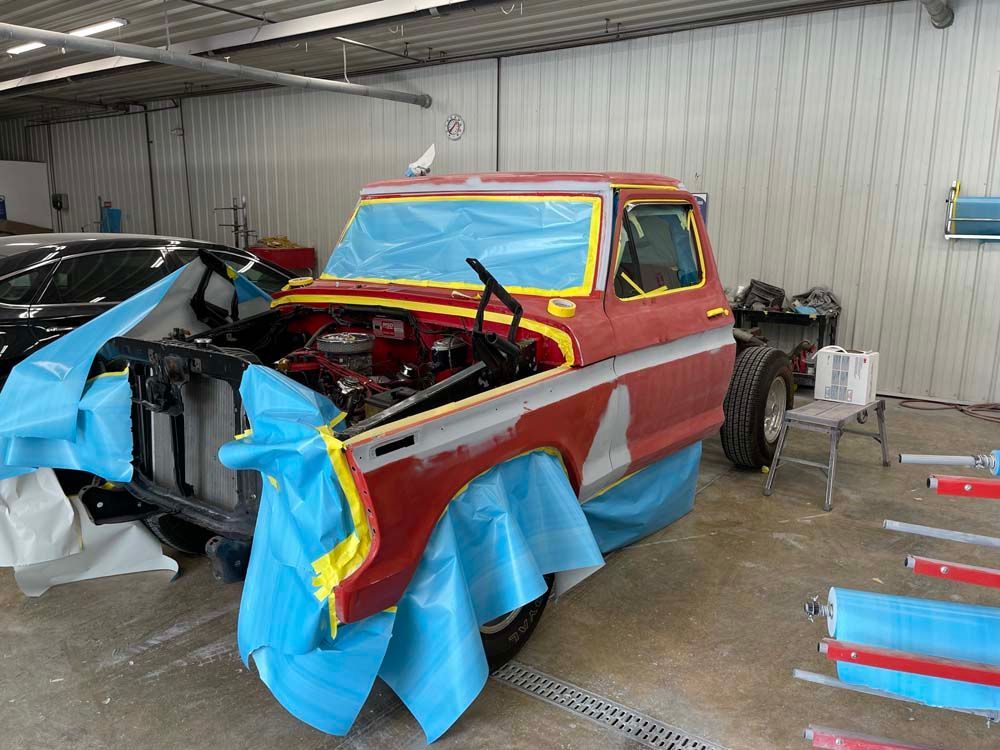 A red truck is being painted in a garage.