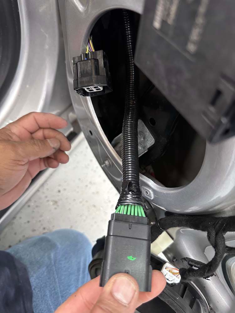 A person is holding a connector in their hand in front of a car door.