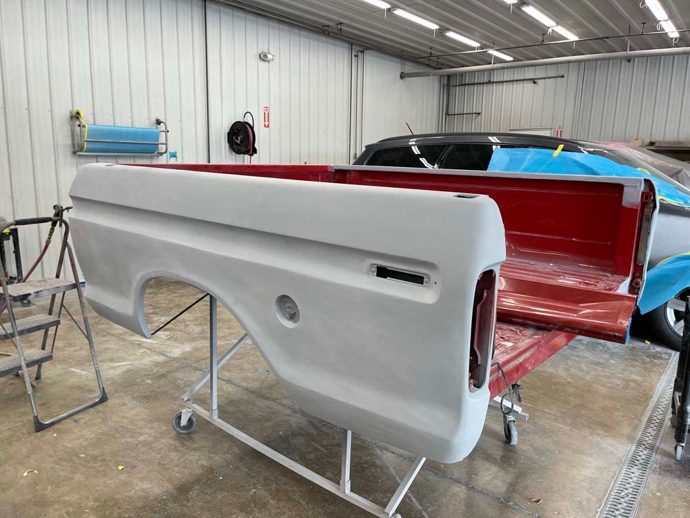 A red truck bed is being painted in a garage.