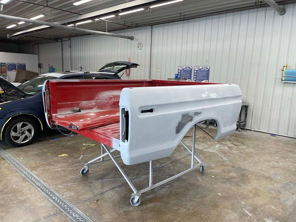 A truck bed is sitting on a cart in a garage next to a car.