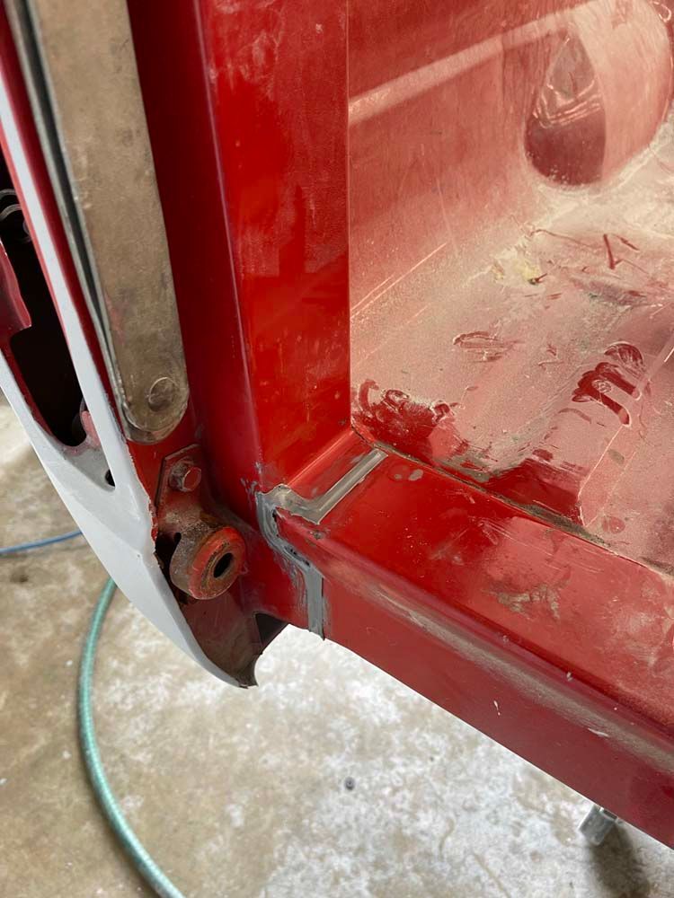 A red car is sitting on the ground next to a hose.