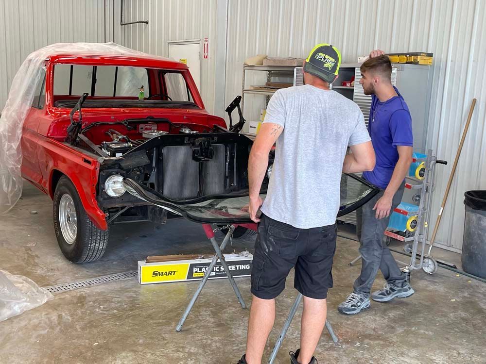 Two men are working on a red truck in a garage.