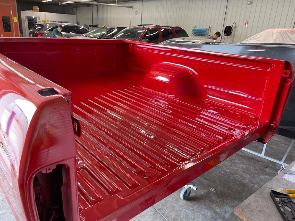A red truck bed is being painted in a garage
