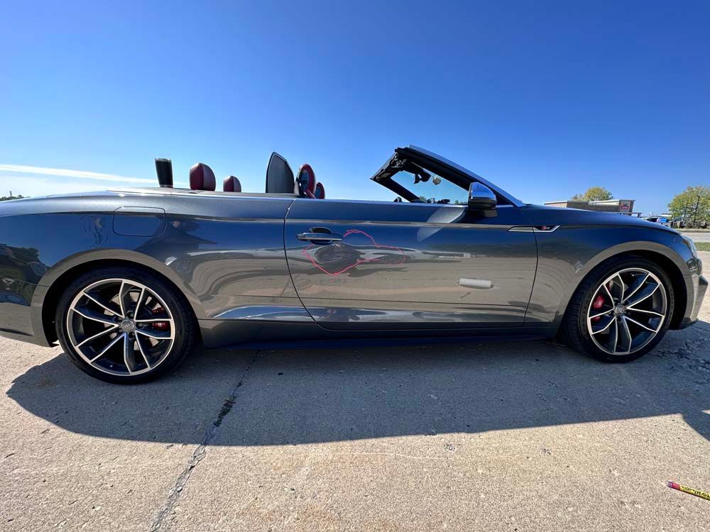 A gray convertible car is parked on the side of the road.