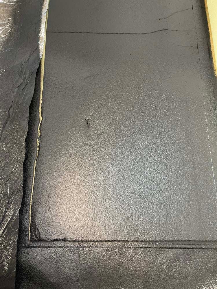 A close up of a black tile floor with a hole in it.