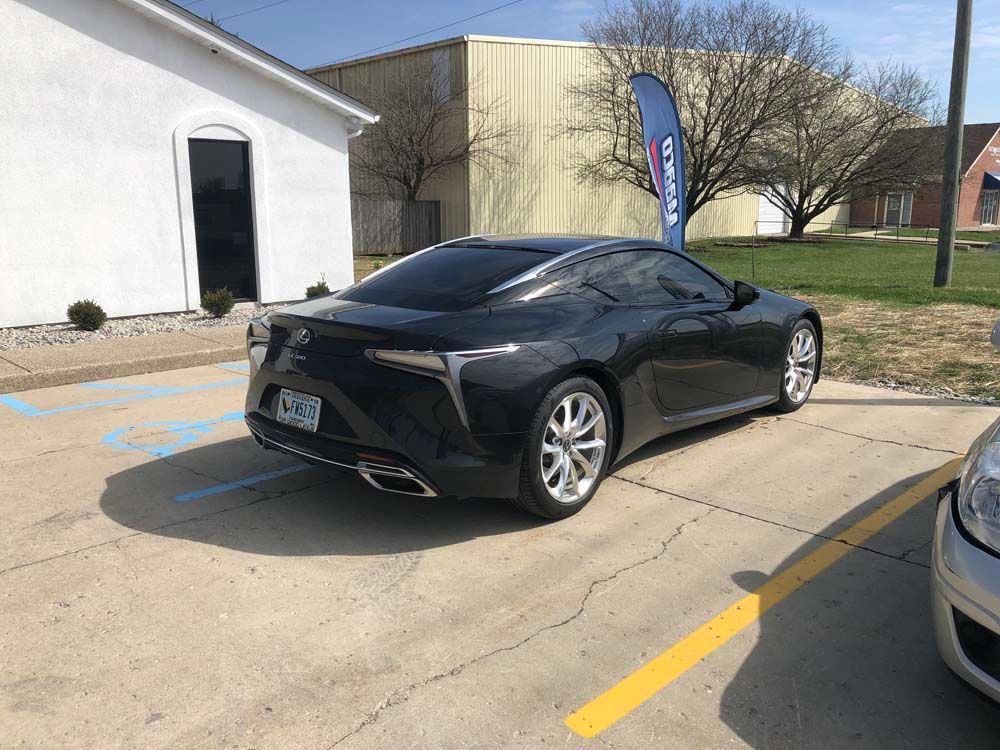 A black sports car is parked in a parking lot in front of a white building.