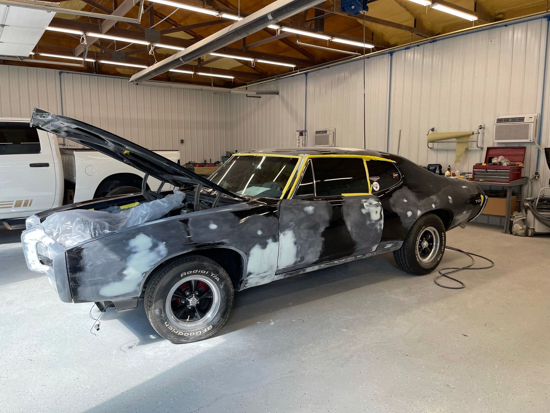 A car is being painted in a garage with the hood up