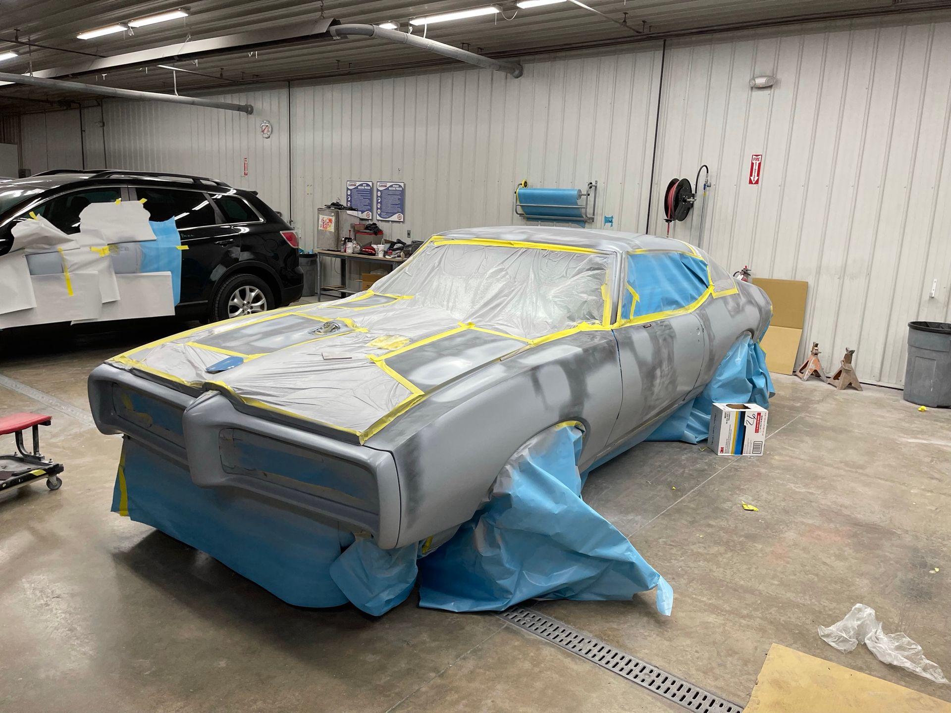 A car is covered in plastic while being painted in a garage.