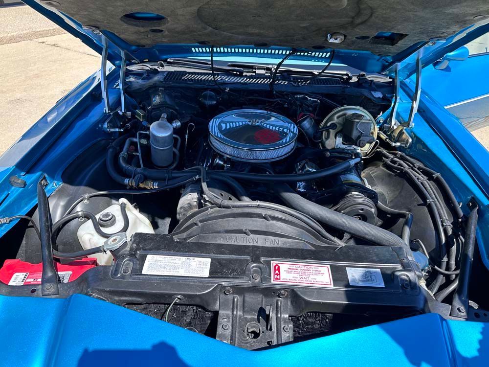 The engine of a blue car is shown with the hood up.