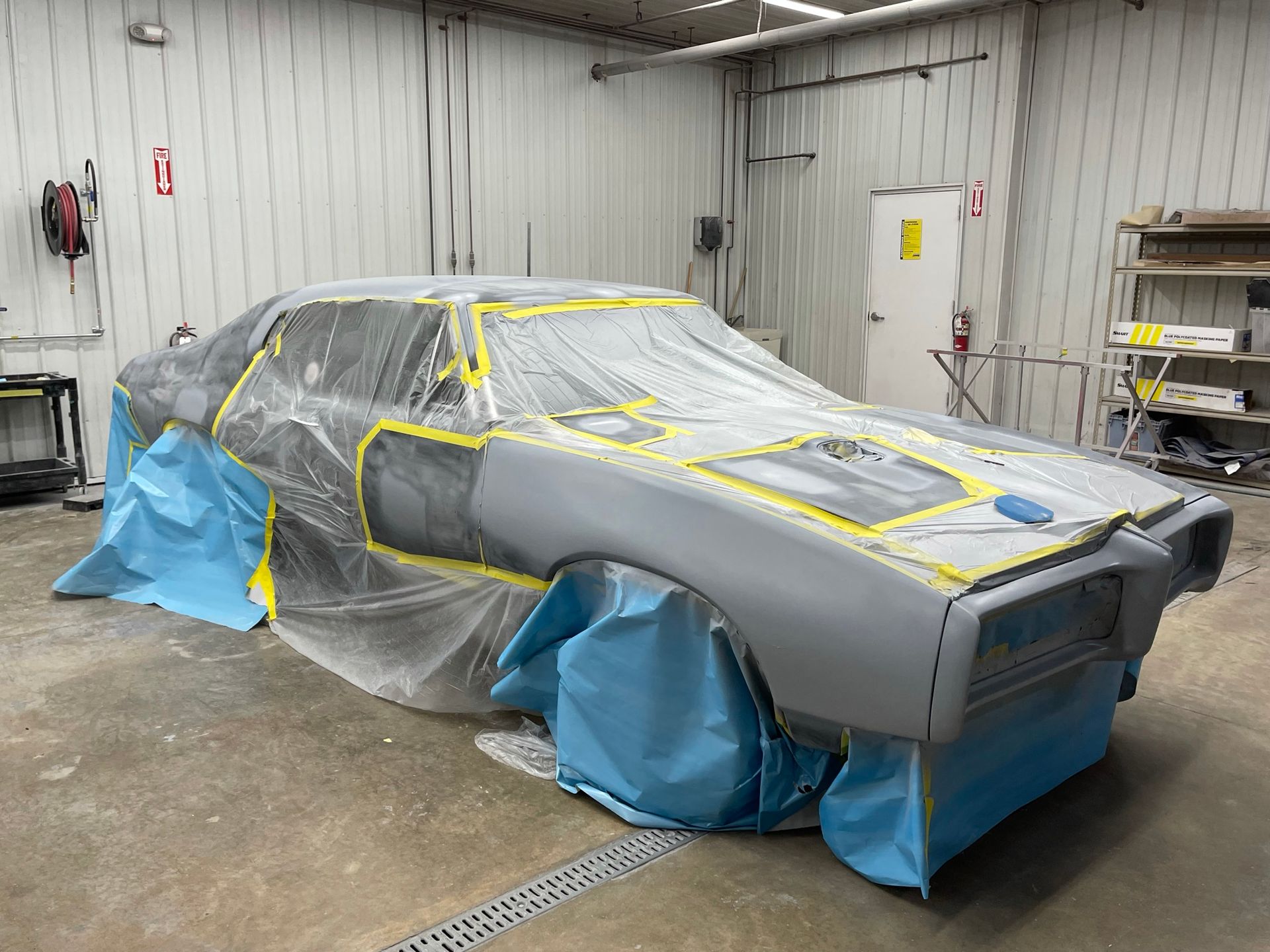 A car is covered in plastic wrap in a garage.