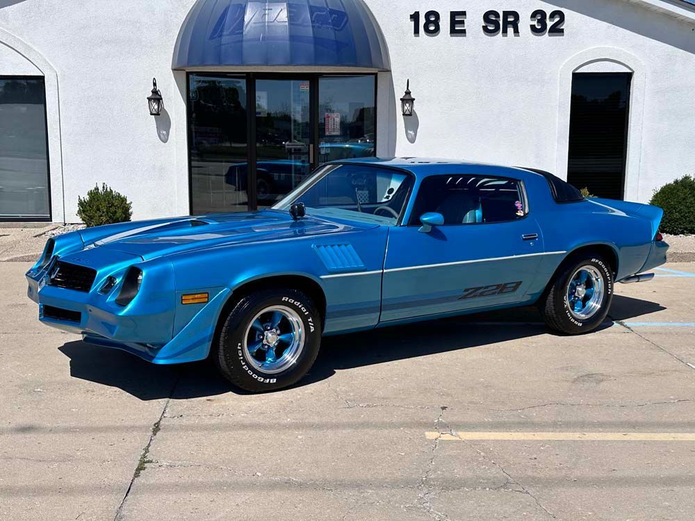 A blue car is parked in front of a white building.