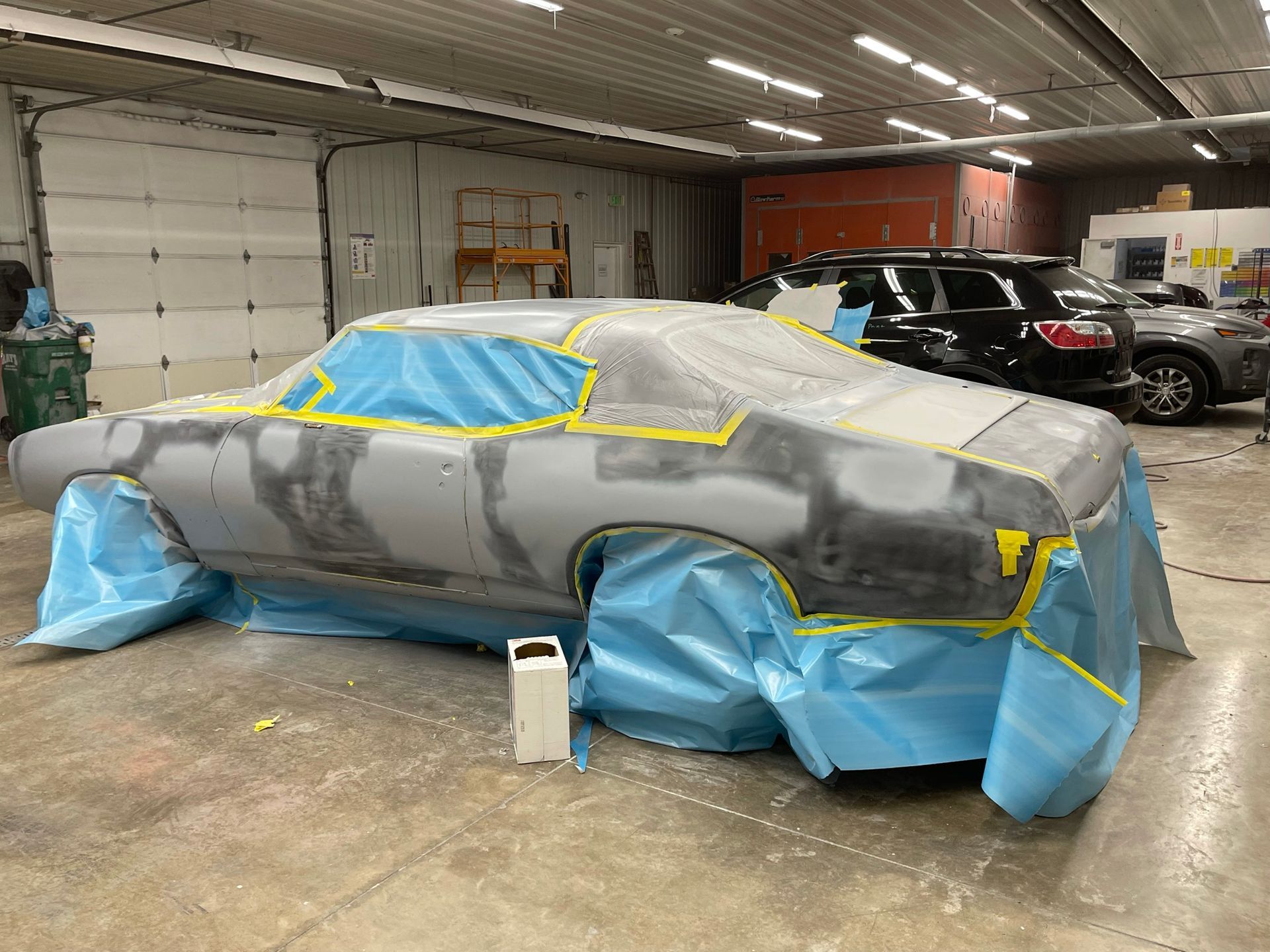 A car is covered in plastic while being painted in a garage.