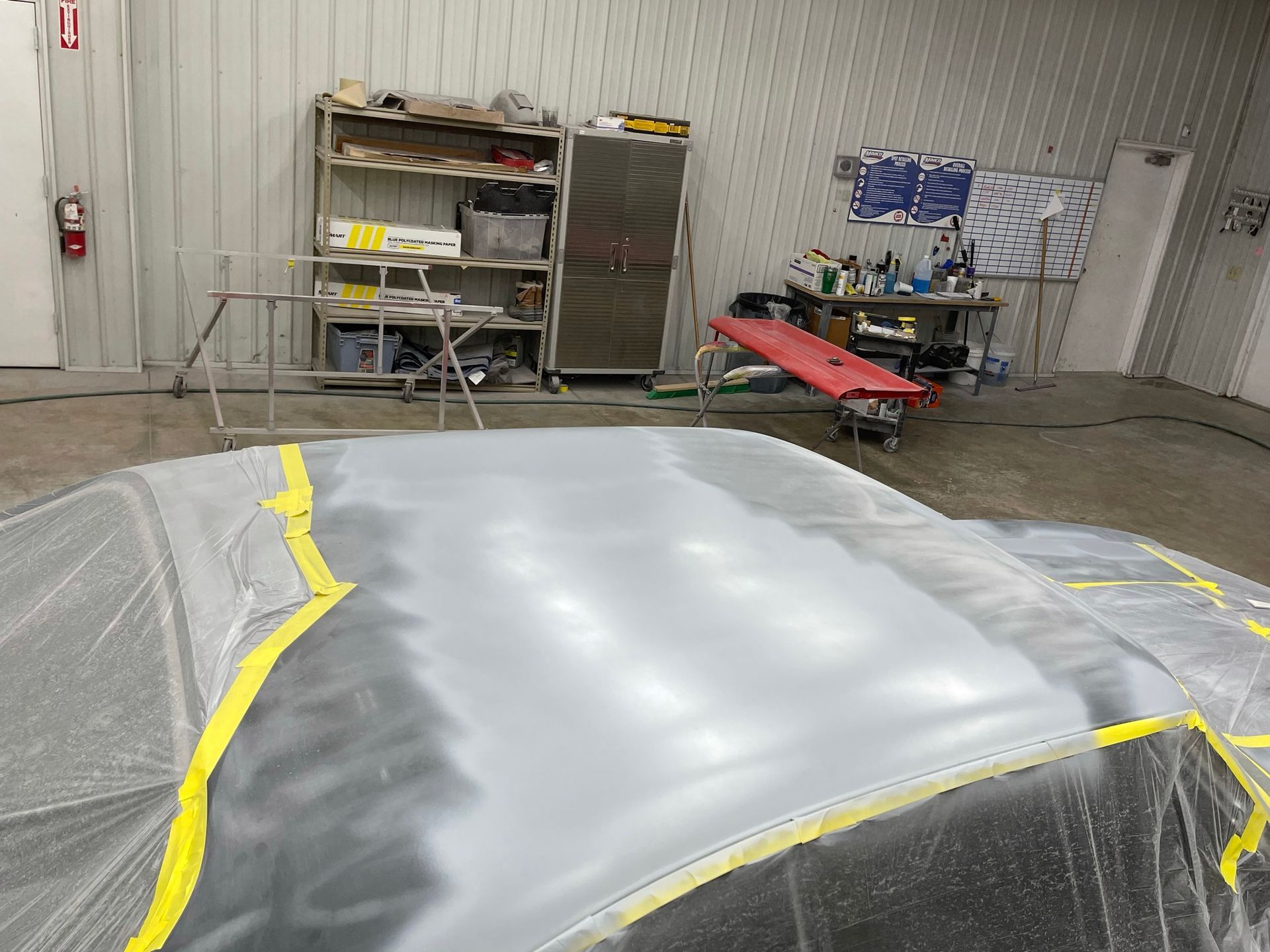 A car is being painted in a garage with yellow tape around it