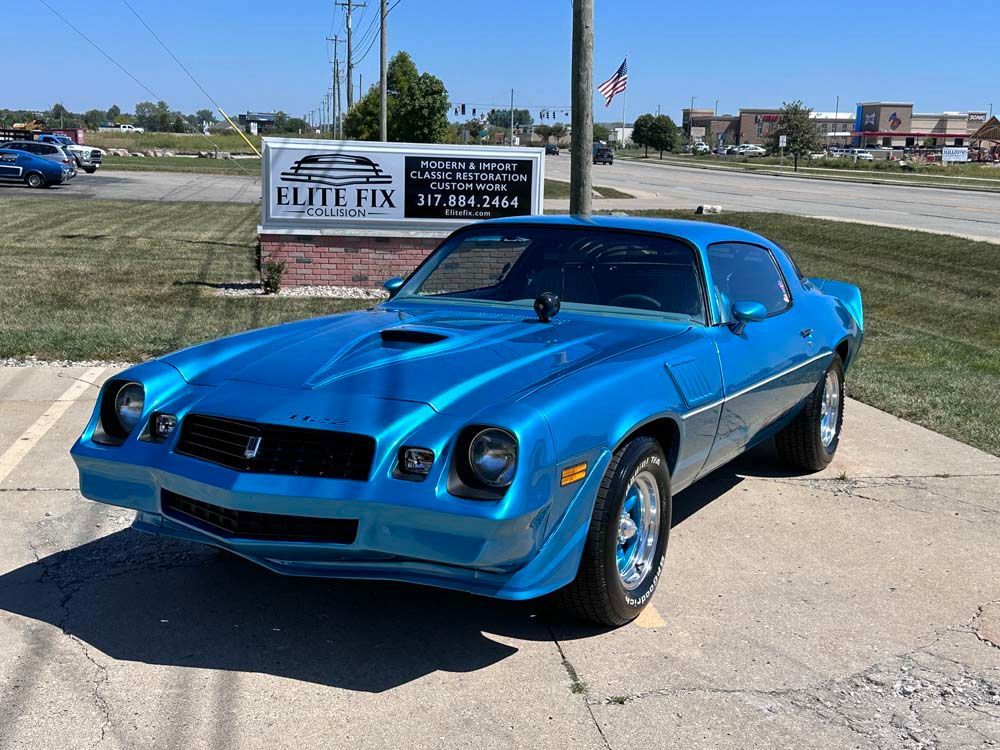 A blue car is parked in a parking lot in front of a sign for elite fix.