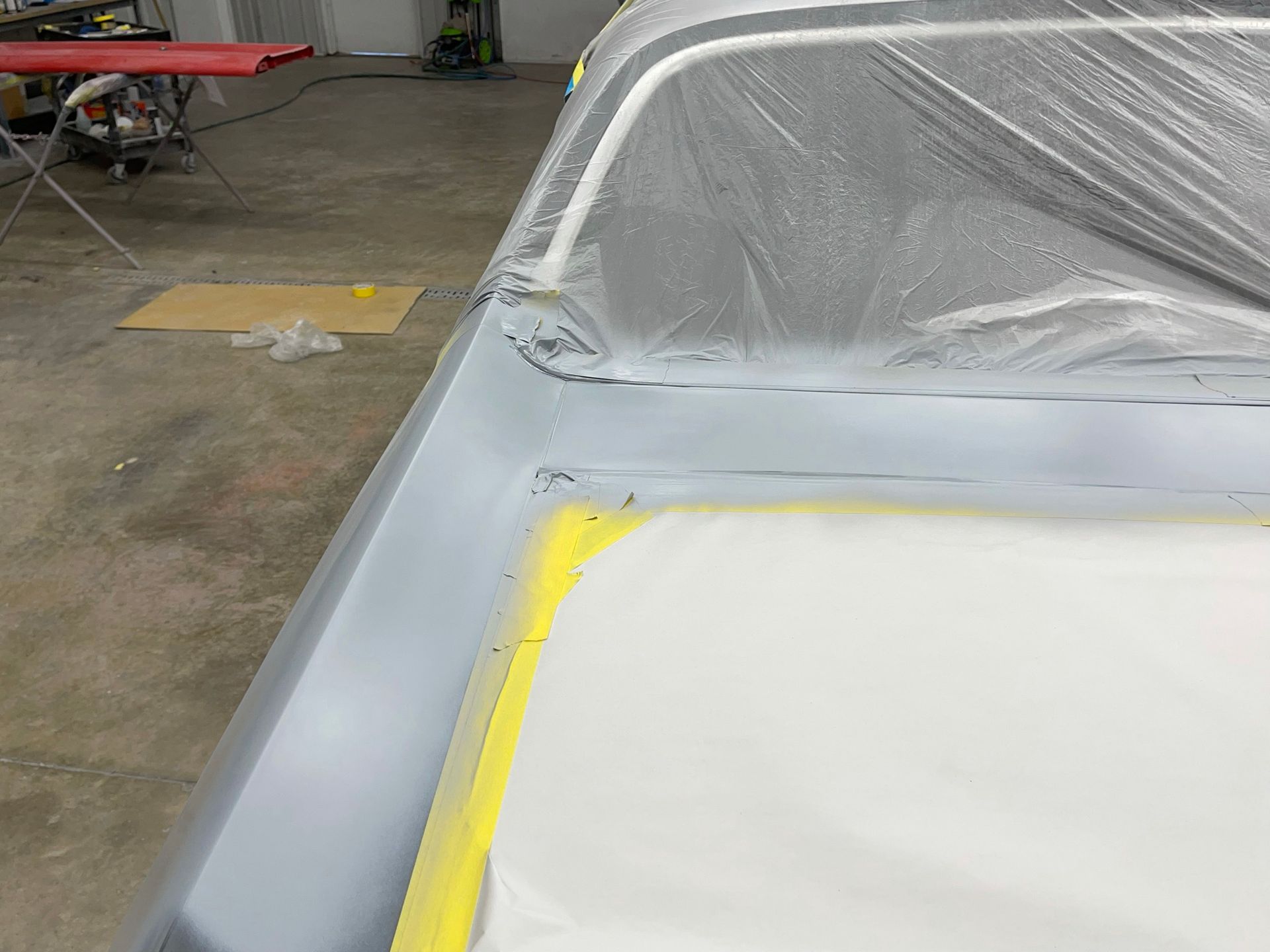 A car is covered in plastic and is being painted in a garage.