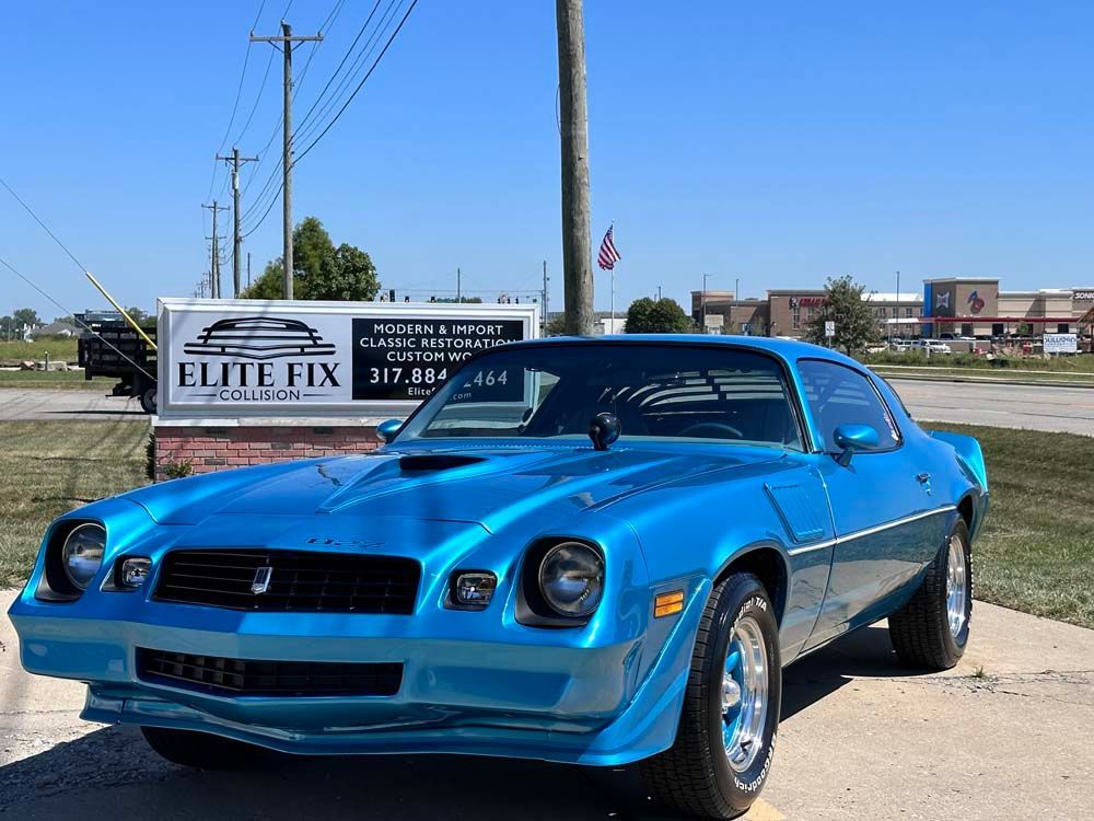 A blue car is parked in front of a sign that says elite fix