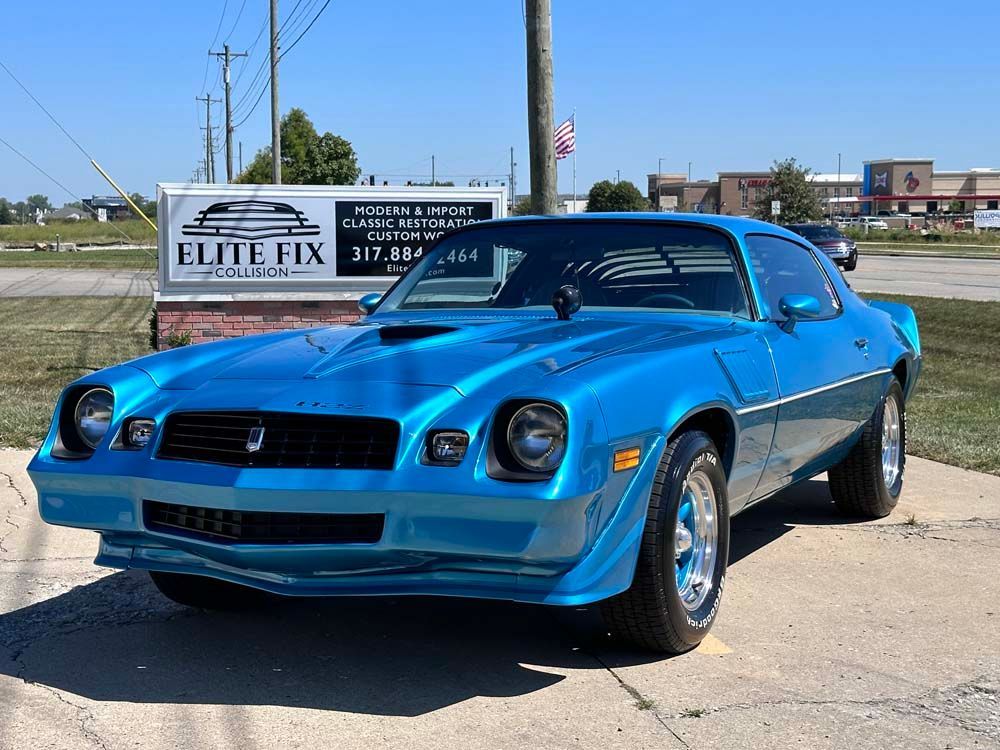A blue car is parked in front of a sign that says elite fix.