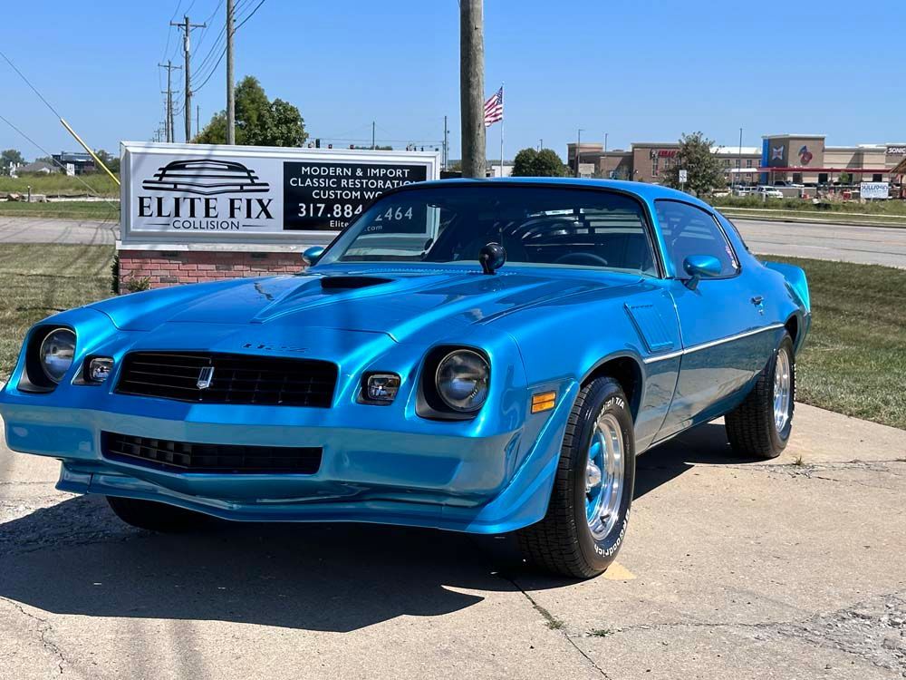 A blue car is parked in front of a sign that says elite fix.