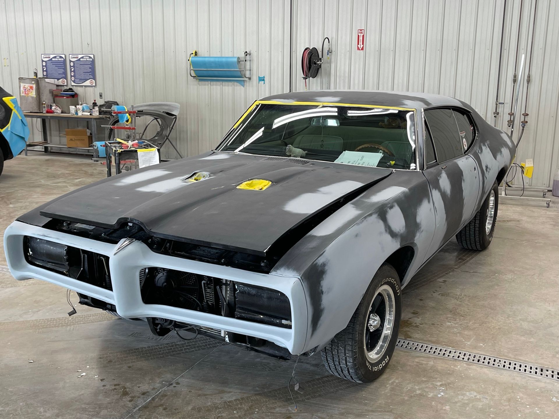 Classic muscle car in a body shop, primed for paint, gray, black, and white.