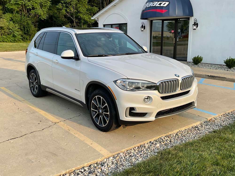 A white bmw x5 is parked in a parking lot in front of a building.