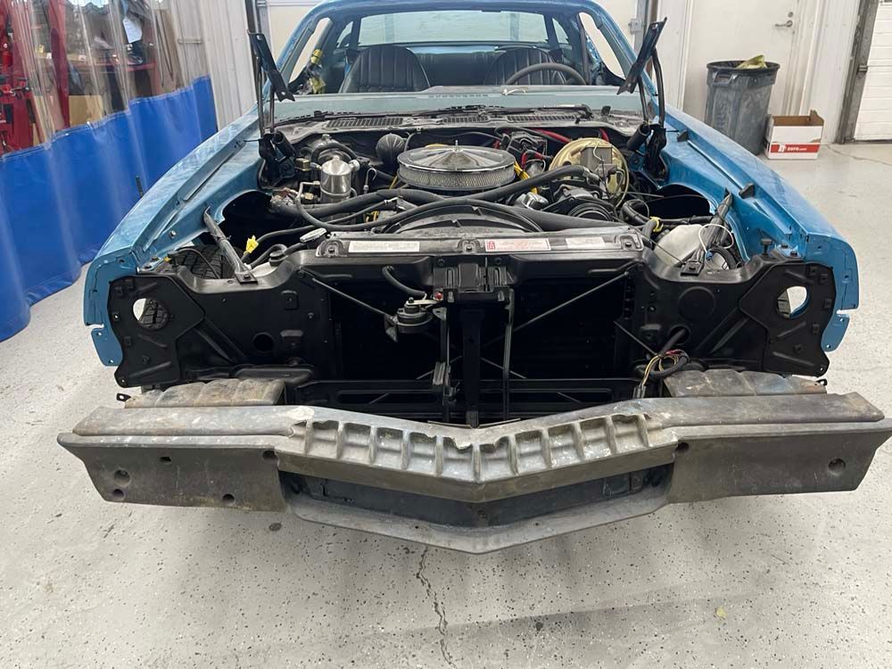 A blue car with the hood up is sitting in a garage.