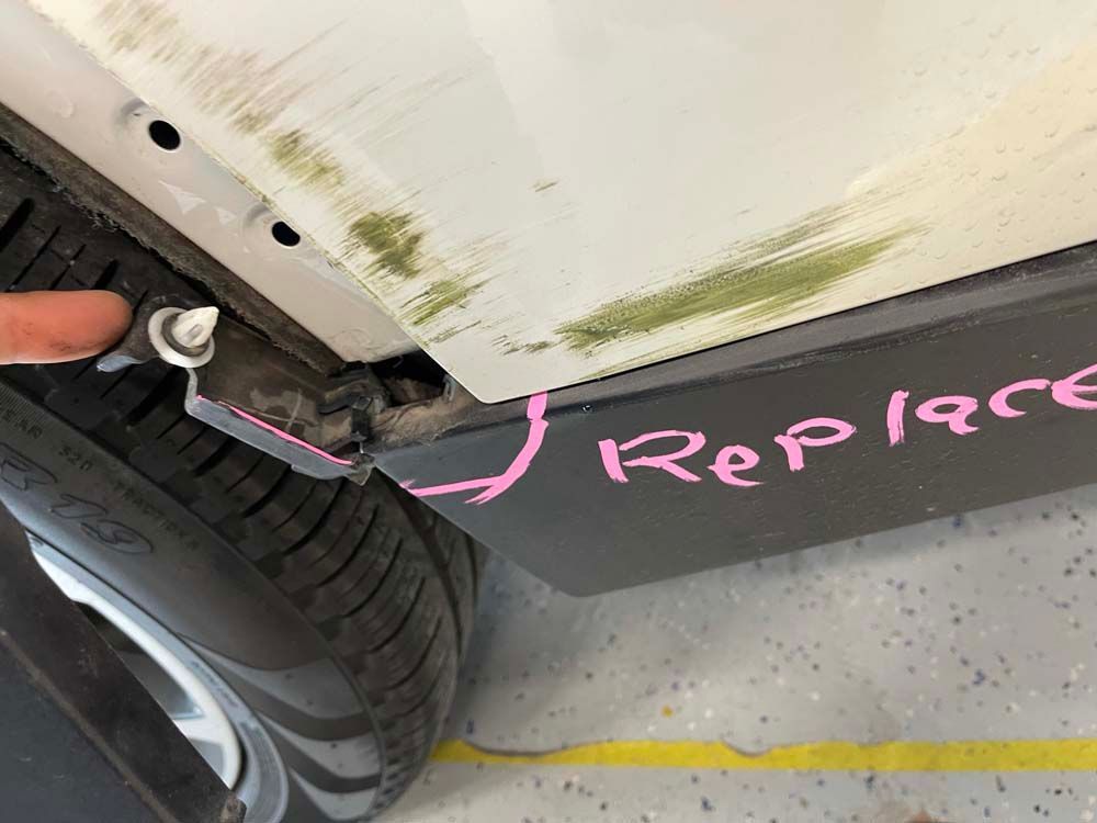 A person is pointing at the side of a car that says replace