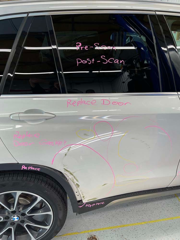 A white bmw x5 with a damaged door is parked in a garage.