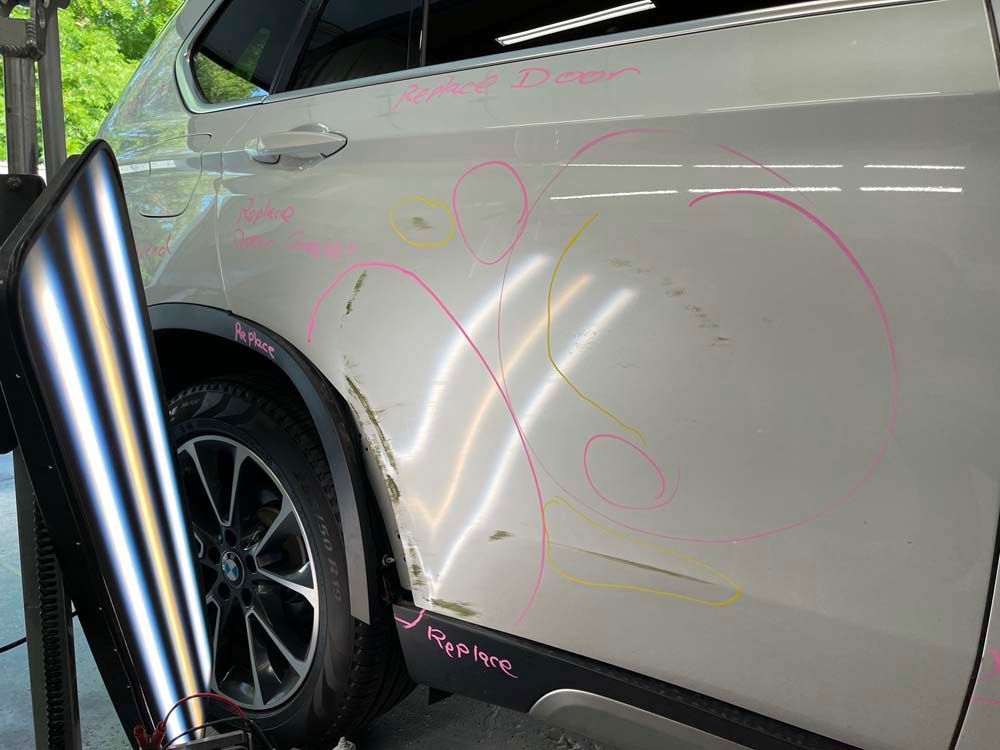 A white car with a damaged door is sitting in a garage.