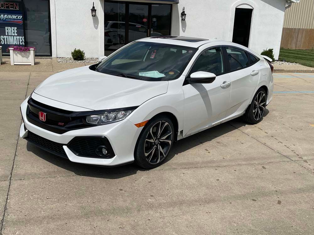A white honda civic is parked in front of a building.