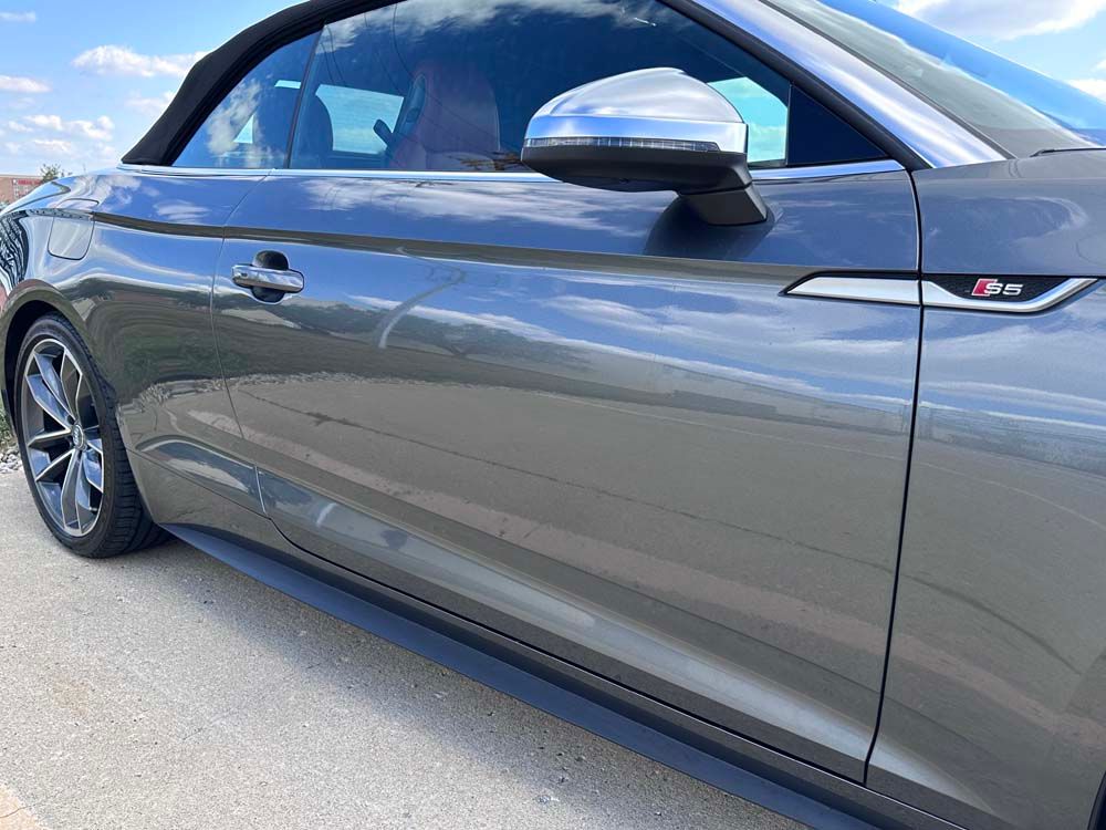 A gray convertible car is parked on the side of the road.