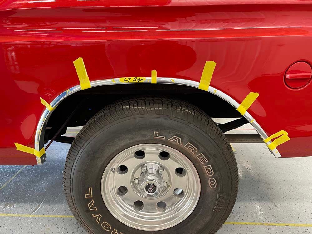 A red truck with yellow tape on the fenders and tires.