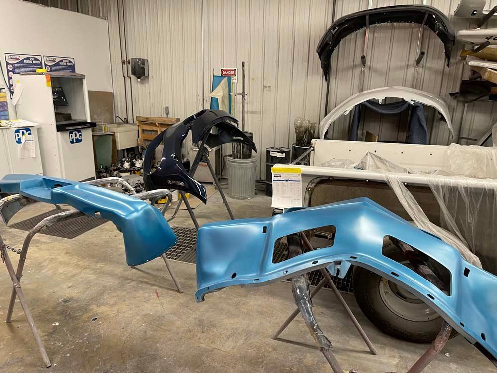 A blue bumper is being painted in a garage.
