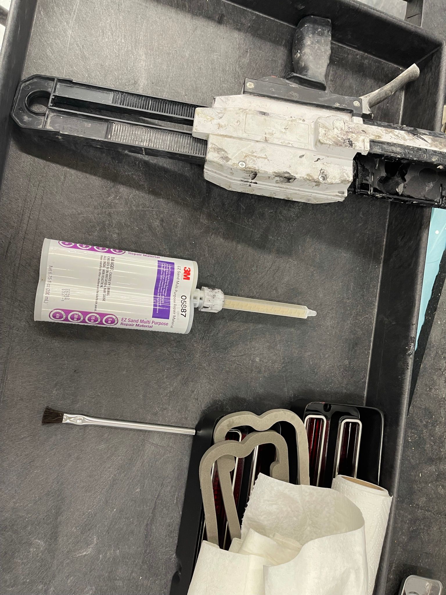 A bottle of adhesive is sitting on top of a tray next to a screwdriver.