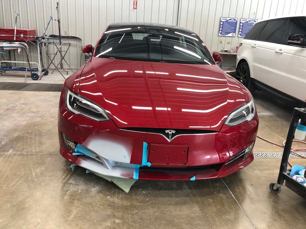 A red tesla model s is being painted in a garage.