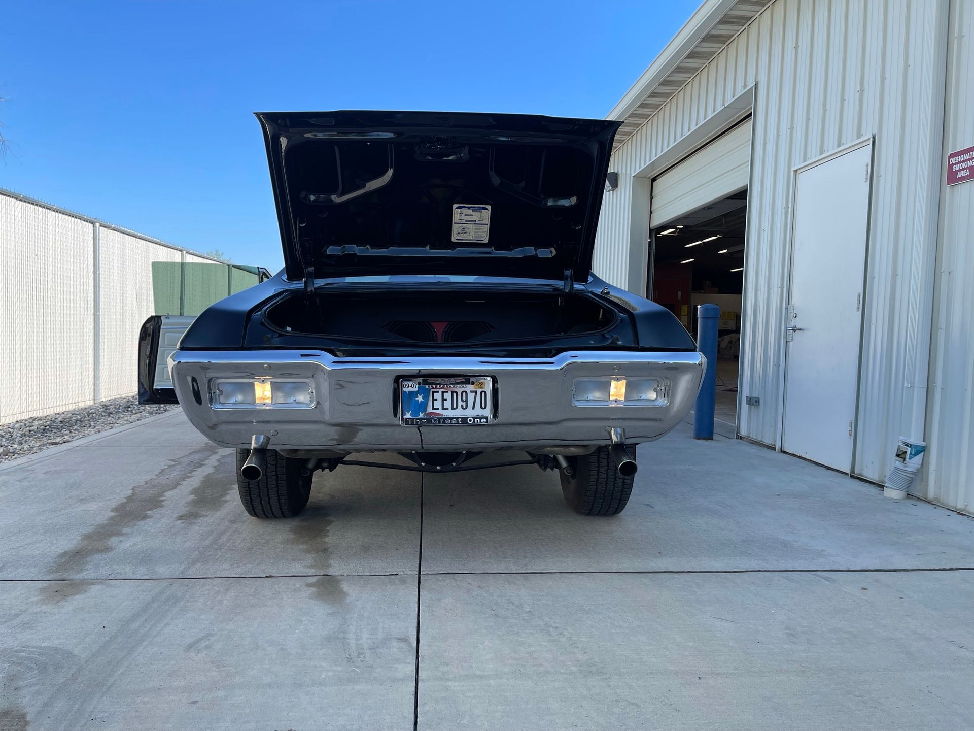 A silver car with the hood up is parked in front of a garage.
