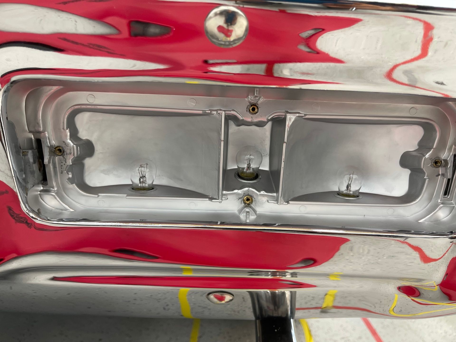 A close up of a chrome bumper with a red car in the background.