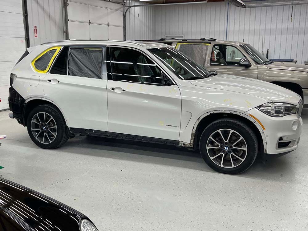 A white bmw x5 is parked in a garage next to a truck.