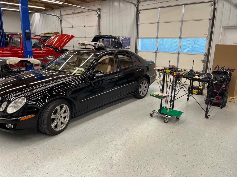 A black car is parked in a garage next to a red truck.