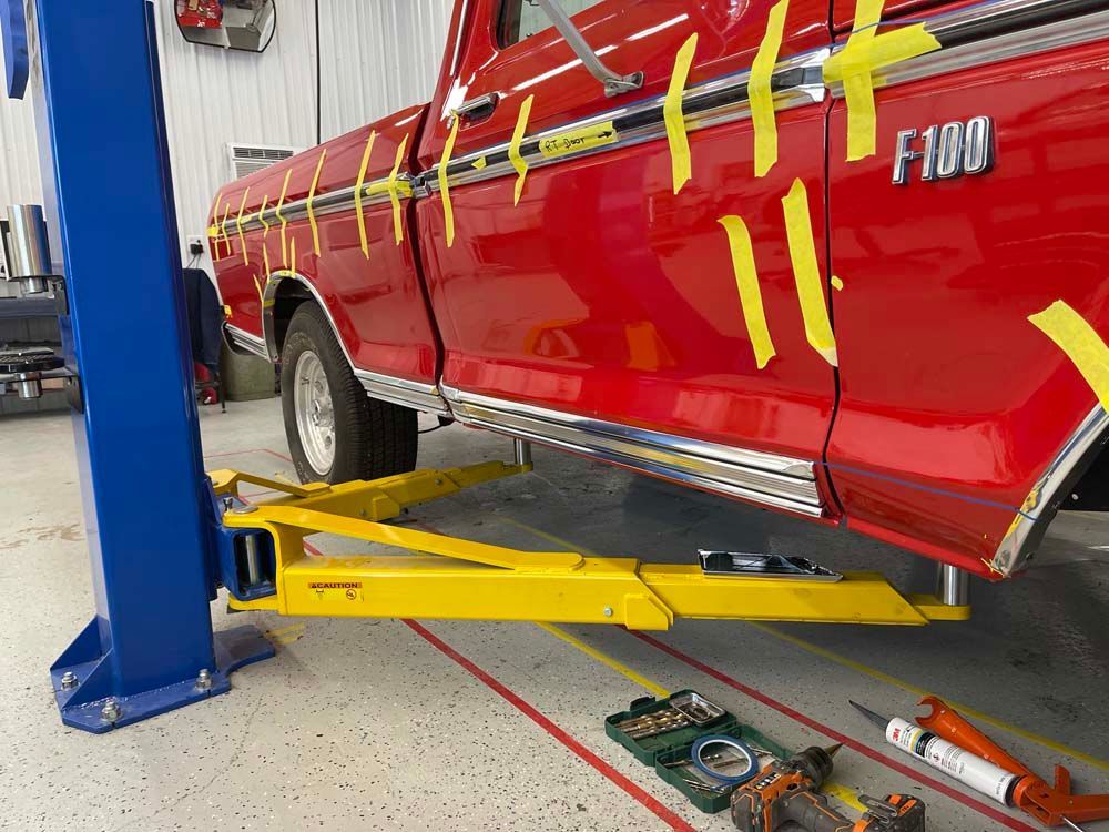 A red ford f100 truck is sitting on a lift in a garage.