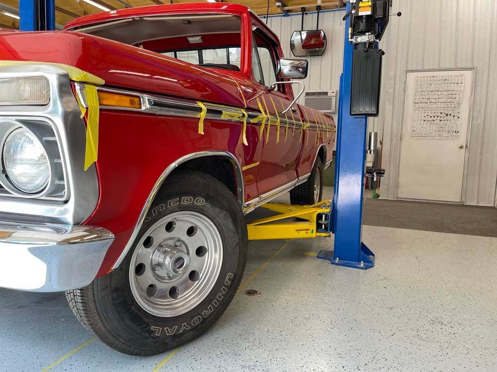 A red truck is on a lift in a garage.