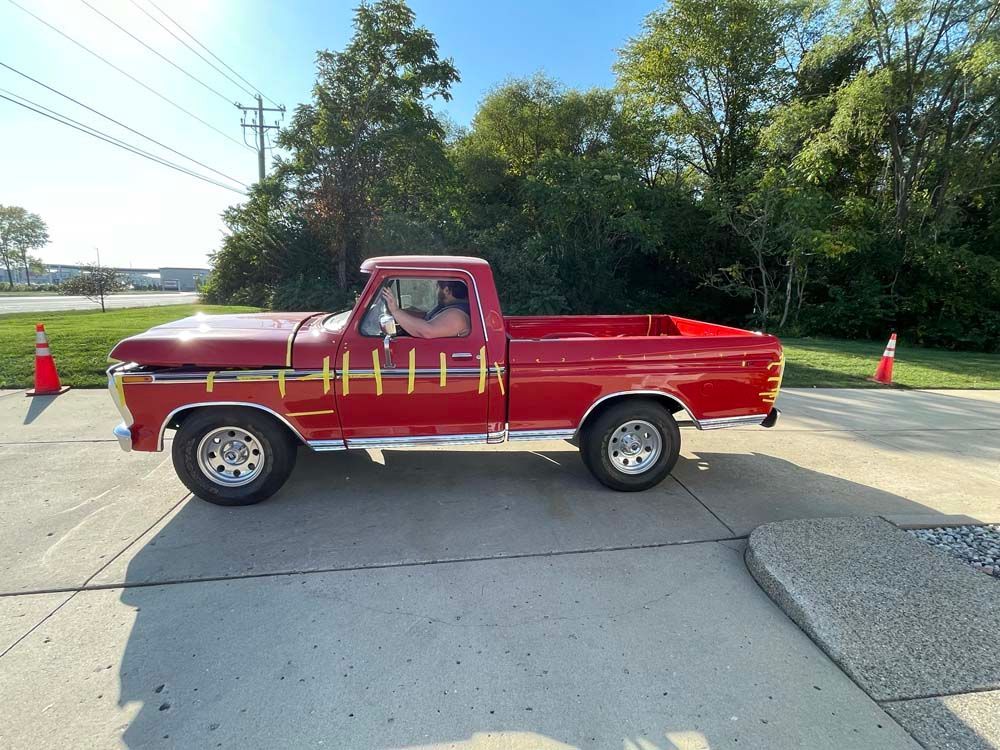 A red truck is parked on the side of the road in a parking lot.