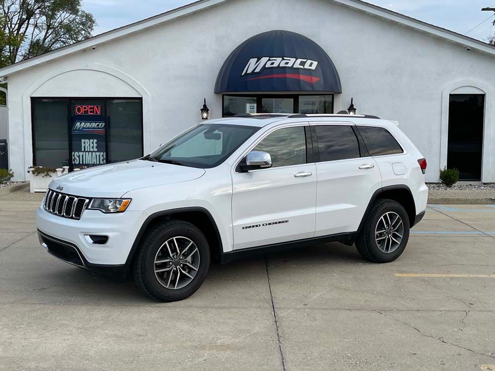 A white jeep grand cherokee is parked in front of a car dealership.