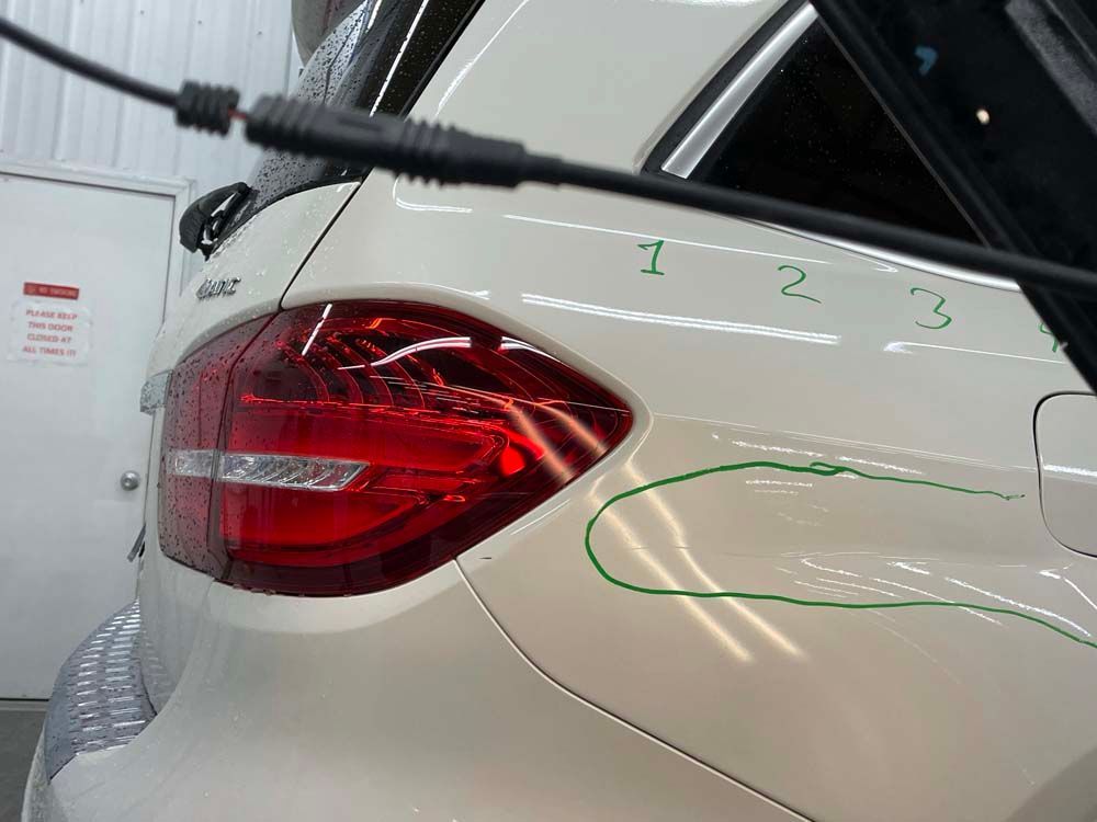 A white car with a red tail light is parked in a garage.