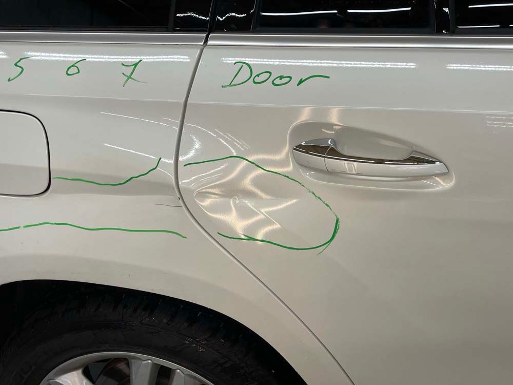 A white car with a damaged door is sitting in a garage.