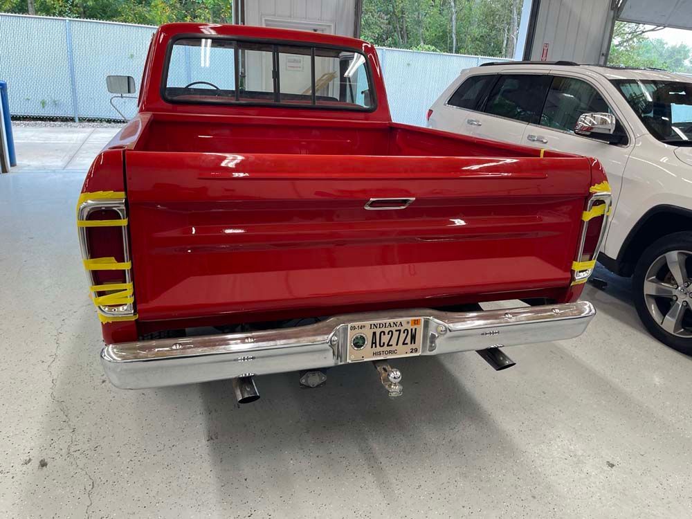 A red truck is parked in a garage next to a white suv.
