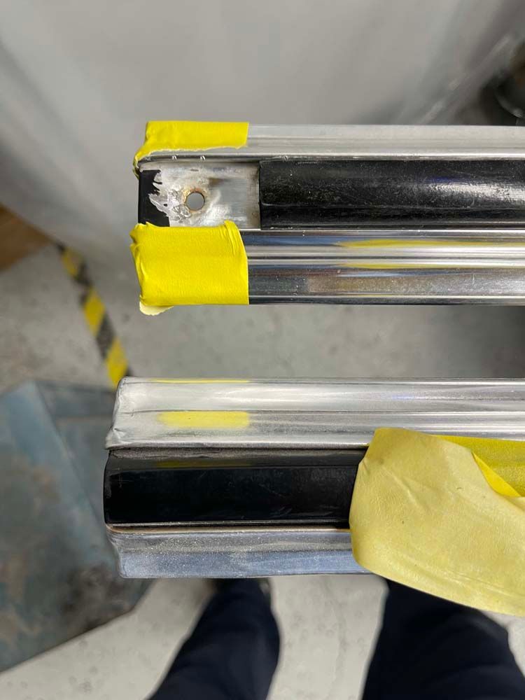 A person is holding a piece of metal with yellow tape on it.