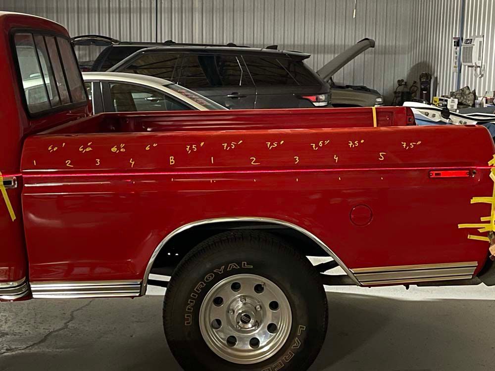 A red truck is parked in a garage next to a silver suv