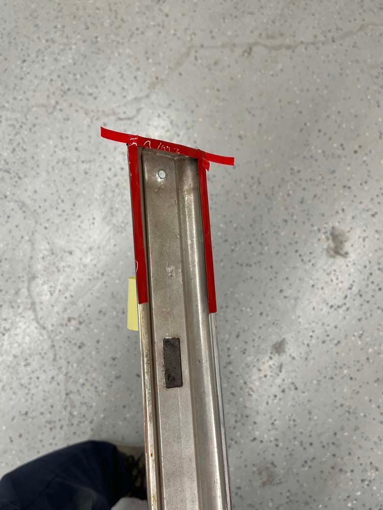 A person is holding a piece of metal with a red tape on it.